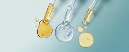 Three different types of droppers filled with serums varying in color on a teal gradient background
