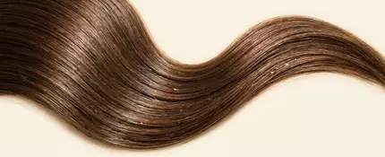 Macro shot of smooth, shiny hair strands arranged on a light background, representing healthy hair after an anti-frizz hair care routine.