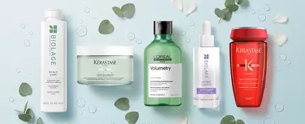 Image of Biolage, Keratase, and L'Oreal shampoo bottles on a light blue background with green leaves, white flower petals, and water droplets