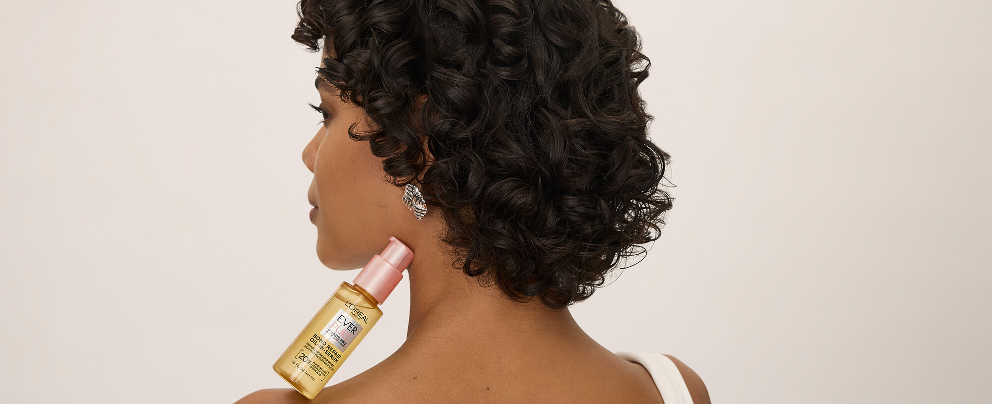 Woman with curly brown hair holding a bottle of Everpure Bonding Serum