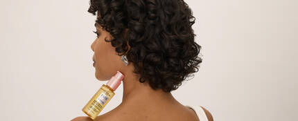 Woman with curly brown hair holding a bottle of Everpure Bonding Serum