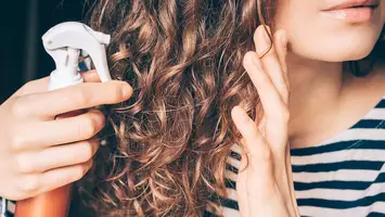 photo of woman applying spray to curly hair