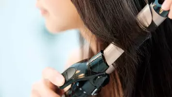 photo of woman curling hair with curling iron