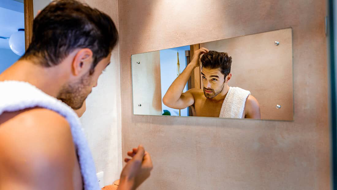 photo of man in mirror styling hair with hair cream