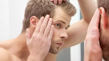 photo of man looking at hair in the mirror