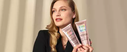 Woman with blonde hair and with two bottles of L'Oreal Paris shampoo and conditioner