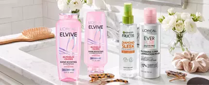 A clean and bright bathroom countertop/sink area featuring various hair accessories like a hair brush, hair clips, comb, scrunchie, etc. Also showing products mentioned in the article like: EverPure Glossing Treatment and Diamond Sleek Spray