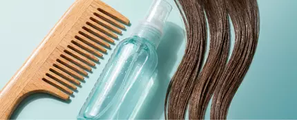 Stylized close-up of a wide-tooth comb and detangling spray resting on a clean surface alongside neatly separated sections of smooth, damp hair swatches in a variety of shades. Drops of conditioner and a soft towel suggest a gentle detangling routine. No people or body parts are present; focus is on hair textures, haircare tools, and moisturizing products.