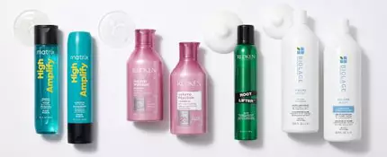 Flat lay showing Matrix High Amplify Shampoo, Matrix High Amplify Conditioner, Redken Volume Injection Shampoo, Redken Volume Injection Conditioner, Redken Root Lifter Volumizing Spray Foam, Biolage Volume Boost Shampoo, and Biolage Volume Boost Conditioner, with texture swatches of shampoo and mousse on a white background.