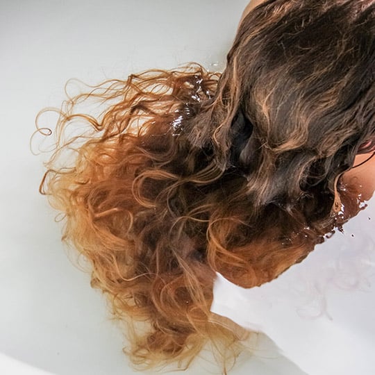 woman's curly hair in a bath tub of water